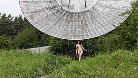 In a public outdoor setting near an old space radar, a brunette with natural tits poses nude