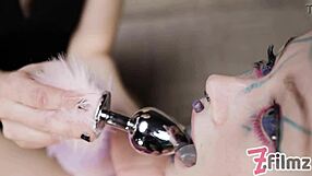 The dominatrix says, 'Obey me, tattoo cat-girl, as I insert the anal butt plug in our lesbian session.'